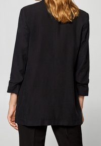 Svart långärmad topp med rak skärning, med en mjuk textur och subtila sömmar, designad för en avslappnad passform och en minimalistisk look.