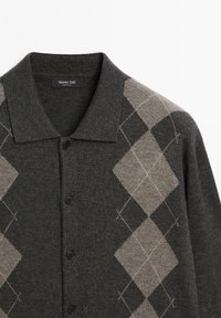 Donkergrijze cardigan met zwarte knopen, voorzien van een ruitpatroon in tinten lichtgrijs en beige aan de rechterkant, gemaakt van zachte stof.