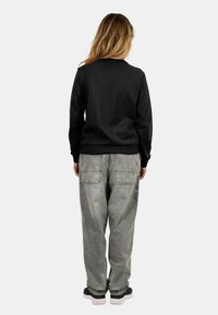 Black sweatshirt with long sleeves, paired with beige baggy jeans featuring back pockets. The model wears dark shoes with light soles.