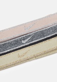 Nike galvas lentes rozā, tumši pelēkā un zelta krāsā ar metāliskām savilkuma detaļām un izšūtām zīmēm, ar mīkstas auduma tekstūru.
