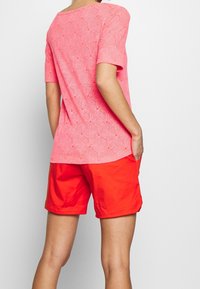 Camiseta rosa con estampado, de manga corta, diseño floral texturizado; combinada con pantalones cortos rojos brillantes. Conjunto de verano sencillo y casual.