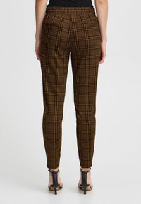 Pantalons en tartan marron avec une taille élastique, coupe fuselée et motif à carreaux discret. Portés avec des chaussures à talons hauts noires à lanières.