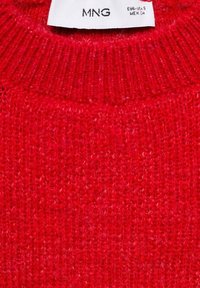 Pull rouge en tricot avec un col côtelé. Le matériau semble doux avec une surface texturée. L'étiquette indique la marque "MNG" et les informations de taille.