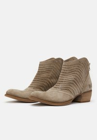 Bottines en daim beige avec motifs découpés, bouts arrondis, petits talons en bois et fermetures éclair latérales pour un enfilage facile.