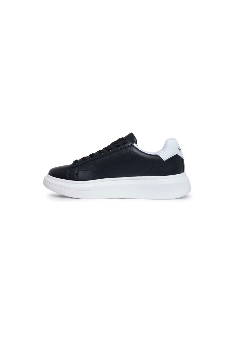 Sneakers in pelle nera con un tassello bianco sul tallone, lacci piatti e una spessa suola in gomma bianca. Texture liscia, design minimalista e senza marchi visibili.