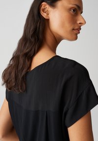 Blusa nera con maniche corte, caratterizzata da una texture liscia e un leggero lucido, che presenta un design con schiena aperta e una vestibilità comoda.