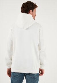 Hvid hættetrøje med en frontlomme, ribbede ærmeafslutninger og en stor hætte. Glat tekstur; tætsiddende silhuet; ensfarvet design uden mønstre.