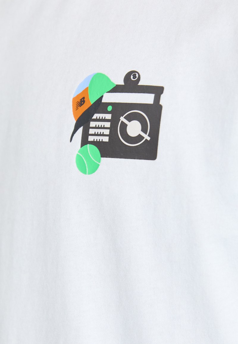 Camiseta blanca con un diseño gráfico de una radio negra acompañada de pelotas de tenis de colores y una gorra, mostrando elementos en verde, azul, naranja y negro.
