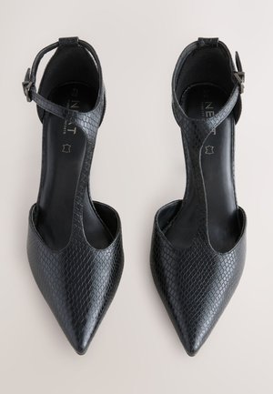 Schwarze spitze Pumps aus strukturiertem Kunstleder. Verfügen über ein offenes Design mit Knöchelriemen und einem niedrigen Ausschnitt. Glattes Innenfutter.