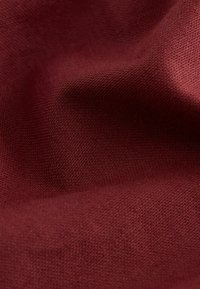 Gros plan d'un tissu texturé froissé de couleur rouge profond avec un motif de tissage visible.