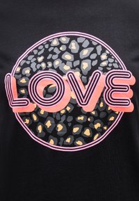 Μαύρο ύφασμα με έναν κύκλο από γκρίζες και μπεζ κηλίδες λεοπάρδας που περιβάλλονται από ροζ περίγραμμα, ενώνονται με γράμματα με ροζ περίγραμμα  που σχηματίζουν τη λέξη LOVE.