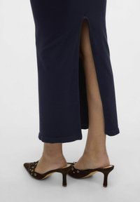 Robe à côtes marine avec une fente latérale, assortie à des mules à talons en daim marron avec des accents décoratifs et des bouts pointus.