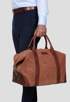 Brun semsket duffelbag med mørkere lærdetaljer, dobbelthåndtak og glidelås. Solid design med romslig innvendig plass.