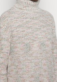 Maglione a collo alto, lavorato a maglia, di colore bianco con macchie multicolori di rosa, grigio e arancione. Design testurizzato con una vestibilità comoda.