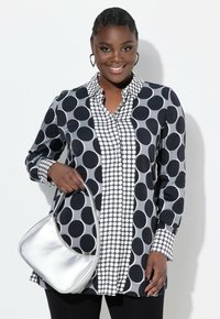 Chemise à manches longues avec un motif à pois noir et blanc, dotée d'un devant à boutons et d'un col rayé contrasté, accompagnée d'un sac à main argenté.