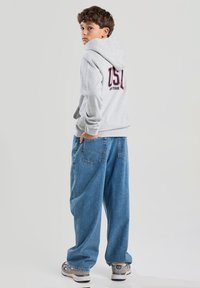 Gray hooded sweatshirt with "USA" in red and blue on the back, paired with loose blue denim jeans, worn by a child.