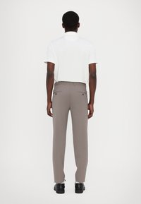 Weißes Poloshirt und graue Slim-Fit-Hose mit Gesäßtaschen und schwarzen Schuhen, von hinten vor einem schlichten Hintergrund betrachtet.