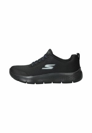 Zapatilla deportiva negra de malla con cierre de cordones en la parte delantera y suela acolchada, con un logo plateado "S" en el lateral y una lengüeta en el talón.