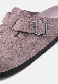 Μαλακό ροζ σουέτ παπούτσι slip-on με ρυθμιζόμενο ασημένιο πόμολο και μαύρη υφασμάτινη σόλα, κοντινή άποψη του πάνω μέρους και του ιμάντα στερέωσης.