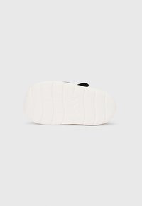 Sandalia tipo slide negra con suela de goma texturizada, con una suela exterior blanca con un patrón ondulado y el logo de la marca. Diseño sencillo y plano.