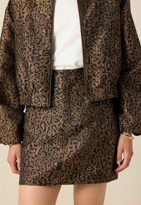 Veste en imprimé léopard brun et noir avec des poignets élastiques, associée à une jupe assortie. Les deux sont en tissu texturé et brillant.