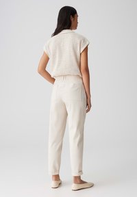 Haut beige tricoté avec des manches courtes, associé à un pantalon crème fuselé avec une taille élastique et des ourlets roulés. Chaussures simples à enfiler.