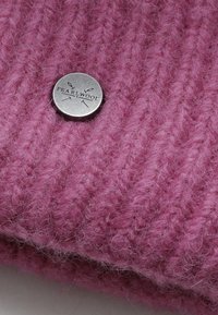 Roze gebreide stof met een zachte, gestructureerde uitstraling; voorzien van een zilveren metalen logoknop gegraveerd met "PEARL WOOL."