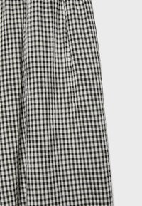 Tissu vichy à carreaux noir et blanc avec des plis subtils et une légère texture visible sur un fond uni.