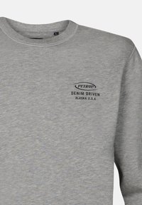 Sudadera gris hecha de un tejido suave. Presenta un logotipo negro que dice "PETROL DENIM DRIVEN ALASKA U.S.A." en la zona del pecho izquierdo. Cuello redondo.