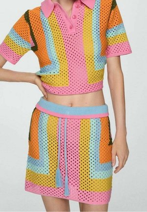 Kvinde iført et farverigt, perforeret strikket to-delt sæt med korte ærmer, en crop top med krave og en højtaljet mininederdel med snøre.