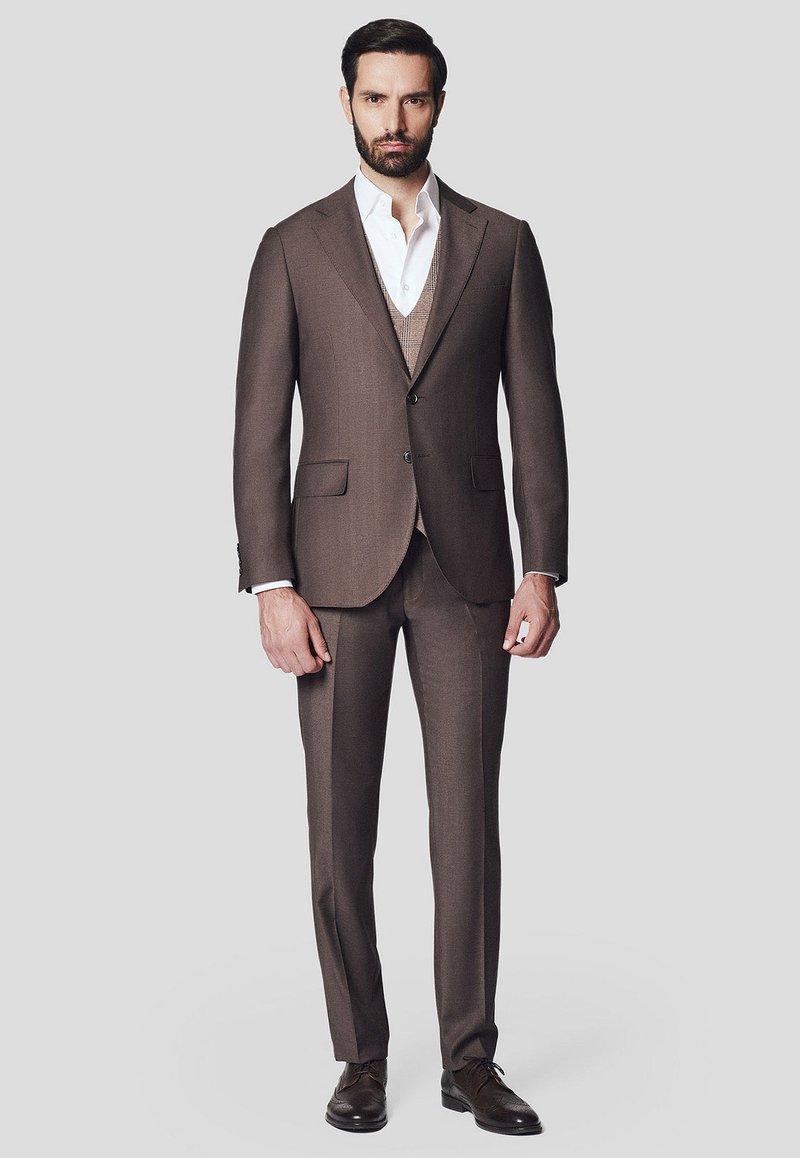Brąski garnitur szyty na miarę z teksturowanym kamizelką, dopasowaną marynarką i pasującymi spodniami. Biała koszula pod spodem, brązowe skórzane buty.