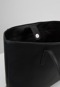 Černá kožená taška přes rameno s texturovaným povrchem, vybavená horním uchopem, zacvakávacím uzávěrem a vnitřní kapsou na zip.