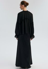 Black flowing dress with long, ruffled sleeves and a high neckline. Sheer accent on cuffs, with a layered design and smooth texture.