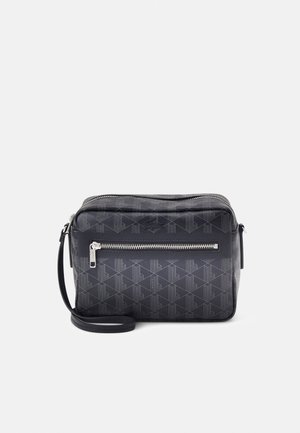 Sac à bandoulière noir avec un motif texturé géométrique, une bandoulière ajustable, une poche zippée à l'avant et une finition lisse.