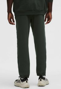 Tmavo zelené tepláky so zúženým strihom a rebrovanými manžetami, v kombinácii s svetlými teniskami s čiernymi akcentmi a textúrovanými vzormi.