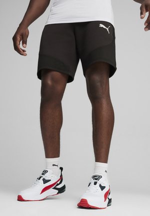 Pantalones cortos deportivos negros con rayas texturizadas, que presentan un logotipo blanco de Puma. Combinados con zapatillas blancas y rojas.