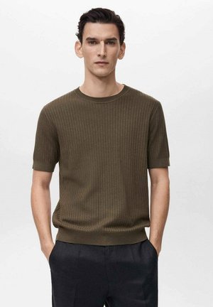 Maglione a maniche corte in maglia ribattuta verde oliva con scollatura rotonda e orlo aderente, indossato da un modello con le mani in tasca.