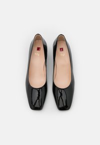 Ballerine in vernice nera con punta quadrata arrotondata e slanciata. L'interno presenta una fodera beige e un piccolo logo rosso. Superficie liscia in tutta la scarpa.
