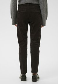 Ruske hirkonukke hlače uskog kroja, s stražnjim džepovima i glatkom teksturom, uparene s crnim kožnim cipelama.