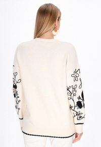 Overgrote crèmekleurige trui met zwarte bloemenborduursels op de mouwen, met een geribde zoom en manchetten. Gladde textuur en een relaxte pasvorm.