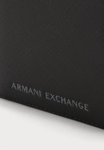 Черна релефна кожена повърхност с брандирано име Armani Exchange, вдълбано с малки, сиви букви близо до ръба.
