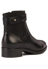 Stivale alla caviglia in pelle nera con finitura liscia, pannello laterale elastico e una cintura decorativa con accessori in tono oro. Tacco a blocco basso.
