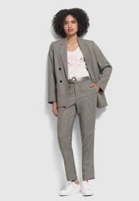 Grijze houndstooth blazer en bijpassende broek, gecombineerd met een wit graphic t-shirt en witte sneakers; heeft een slim-fit ontwerp en een riem.
