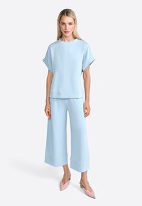 Light blue oversized short-sleeve top paired with wide-leg trousers, both in a soft fabric. Pink pointed-toe shoes complement the outfit.