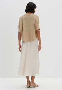 Beige gestricktes Oberteil mit kurzen Ärmeln, kombiniert mit einem fließenden weißen Maxirock. Glatte Textur, lockere Form und leicht asymmetrischer Saum.