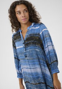 Modra obleka z vzorcem, ki vključuje ovratnik, zadrgo in dolge nabrane rokave. Poudarki z zlatimi madeži in črnimi črtami. Lahka tkanina.