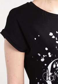 Camiseta de algodón negra con mangas enrolladas y diseño de salpicaduras blancas. Presenta un logo circular en impresión reflectante en el frente.