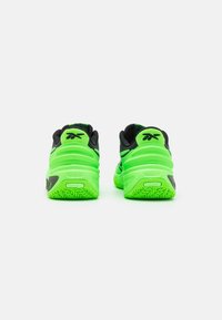 Grüne und schwarze Sportschuhe mit einer strukturierten Gummisohle, gepolstertem Kragen und kontrastierenden Designelementen an der Ferse und an den Seiten.