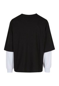 Oversized sort t-shirt med korte ærmer, der har et hvidt langærmet lag nedenunder. Fremstillet af bomuldsstof, enkel design, minimal detaljering.