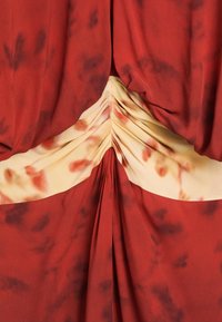 Red and beige tie-dye fabric with a ruched design gathered at the center creating folds and a soft texture.